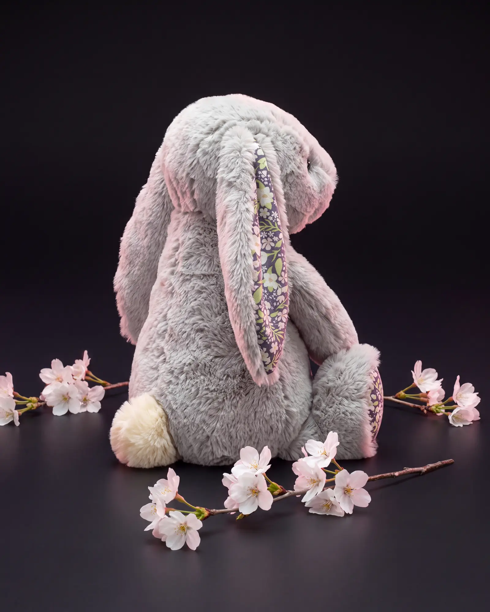 白とピンクの桜の枝のあいだで、肩越しに背を向け、クリーム色のしっぽを見せるうさぎ。